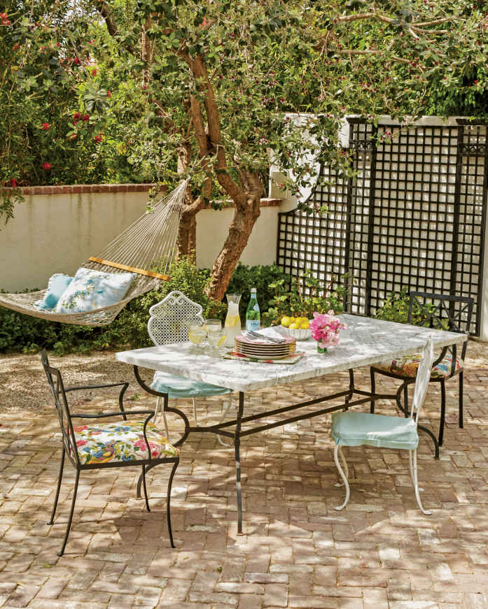 ONE LUMP OR TWO? This newly installed, open patio is the perfect scene for kid-friendly, adult-size tea parties with its pale bricks (laid in a formal herringbone pattern), marble-top dining table, and pillow-filled hammock.